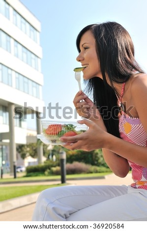 Young beautiful woman having lunch break and eating salad outdoors with building in background