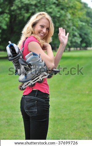 Young smiling woman with roller skates giving good bye gesture with hand. Outdoors in park.