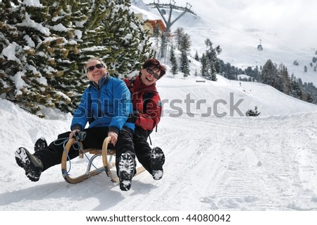 Active senior couple on sledge having fun in mountain snowy country