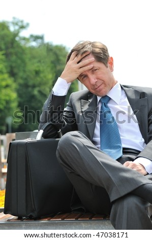 Portrait of depressed and worried senior business man siting on bench outdoors
