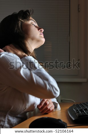 Neck pain - young tired business woman working overtime at computer, night setting
