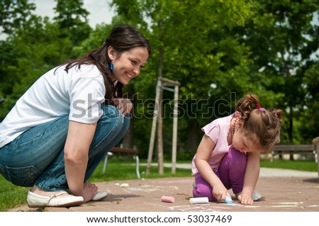 Mother is watching her cute daughter drawing with chalk on sidewalk