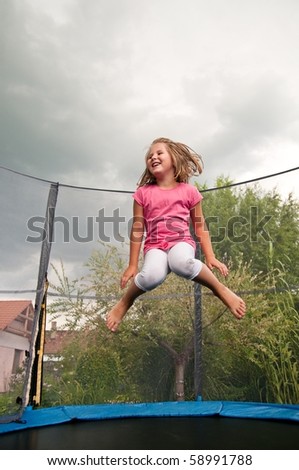 Small cute child jumping on trampoline - garden and family house in background