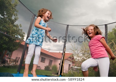 Small cute children jumping on trampoline - garden and family house in background