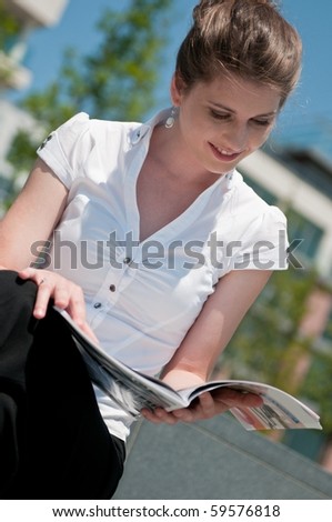Young business woman sitting outdoors reads magazine