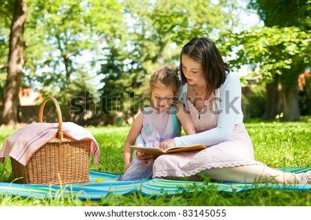 Mother and child reading book on picnic in park