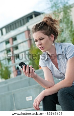 Young worried woman with unhappy expression holding mobile phone - outdoors in urban setting