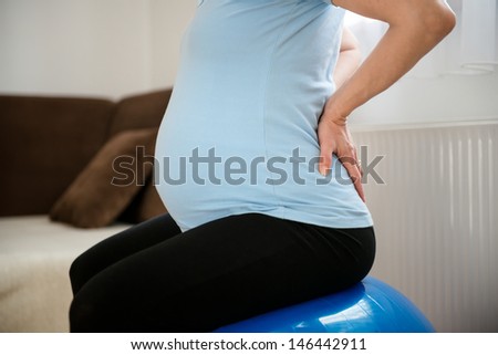 Torso of pregnant woman sitting on fit ball with backache
