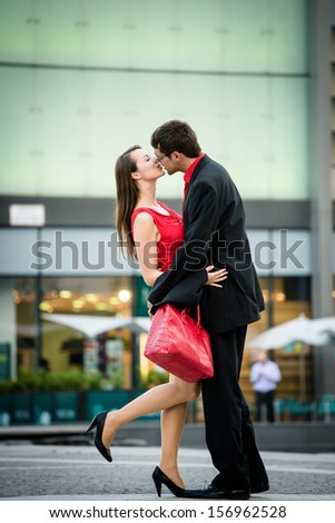 Young business couple dressed in red kiss and welcome each other on street