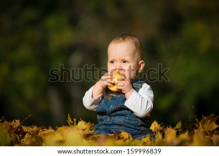 Cute baby eating apple outdoor in autumn nature - sitting in leaves