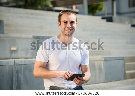 Young man reading book on electronic book-reader in urban environment