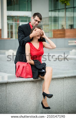 Young business man covering eyes of waiting woman and hiding behind her