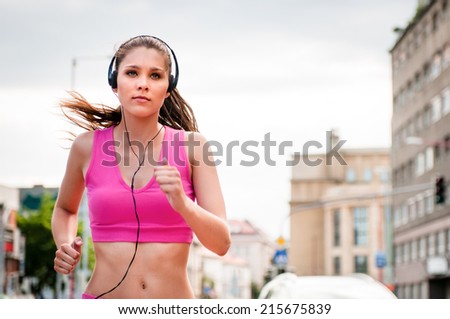 Young beautiful woman with headphones jogging and listening music in street