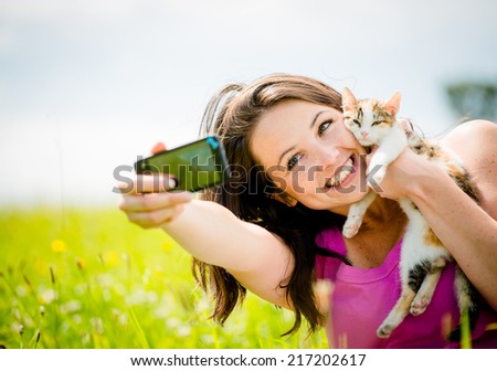 Woman taking photo with mobile phone camera of herself and her cat - outdoor in nature