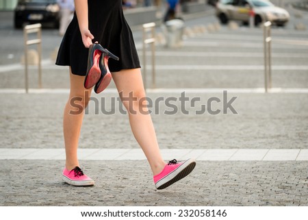 Young woman  walking down street in sneakers and high heels shoes holding in hands