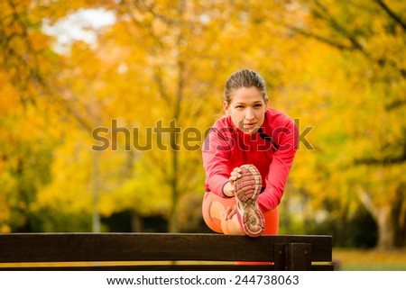 Young woman stretching her leg on bench before jogging in autumn nature