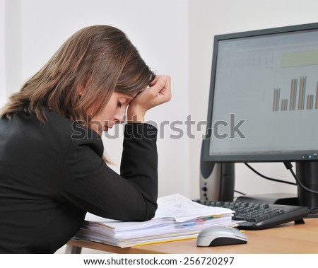 Tired young business woman in depression sitting at computer on workplace