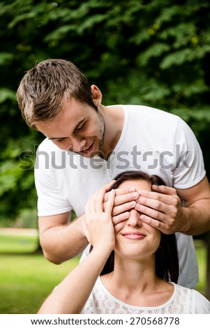 Young man covering with hands eyes of young beautiful woman - outdoor