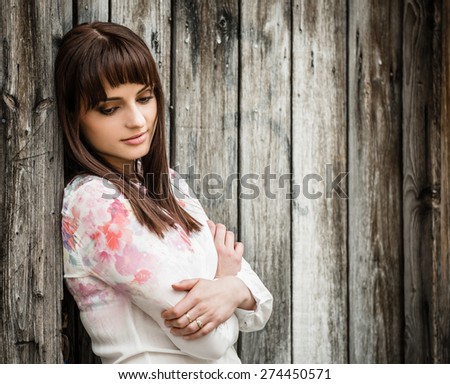 Portrait of smiling woman looking down holding her shoulder - leaning at wooden fence