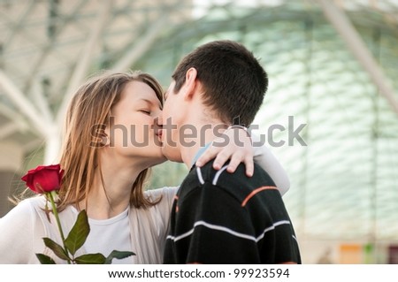 Young man handing over a flower (red rose) to woman and kissing her