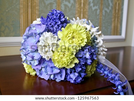 Wedding bouquet of yellow carnation, blue and white hyacinths, blue hortensia lying on wooden table