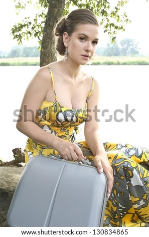 Tired young woman with traveling bag, resting under tree on hot summer day