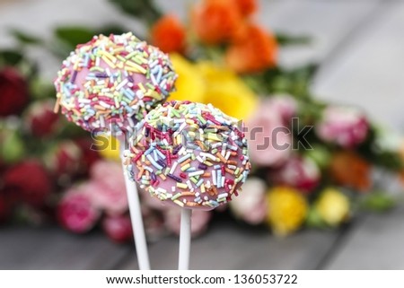 Pink cake pops lavishly decorated with sprinkles on flower background
