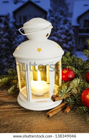 Beautiful white lantern on snowy evening landscape. Christmas decorations on rustic wooden table.