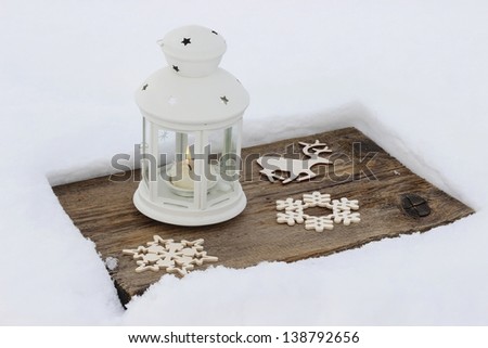 White lantern standing on wooden board, on snow