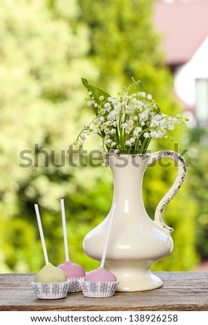 Lilly of the valley flowers and pastel cake pops on wooden table in summer garden.