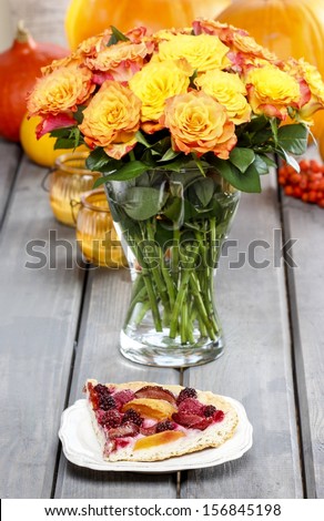 Piece of cake and huge bouquet of orange roses on wooden table. Ripe pumpkins and rowan berry in the background. Autumn party decor.