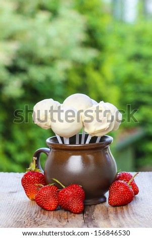 Jug of white cake pops, fresh strawberries around. Summer garden party.