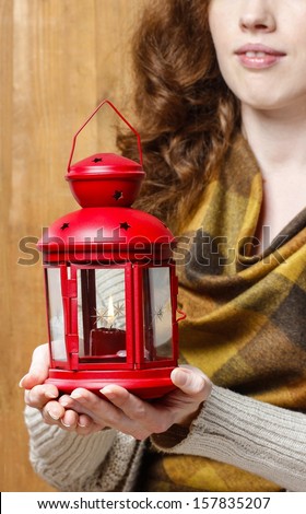 Woman holding red christmas lantern. Wooden wall in the background