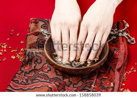 Woman in a nail salon receiving a manicure, she is bathing her hands in water with rose petals