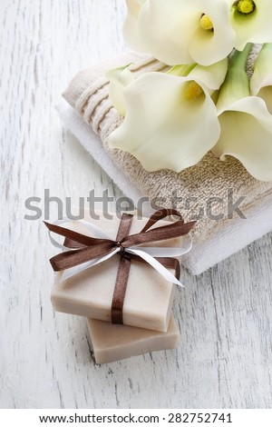Bar of handmade natural soap, towels and bouquet of white calla flowers on rustic wooden table