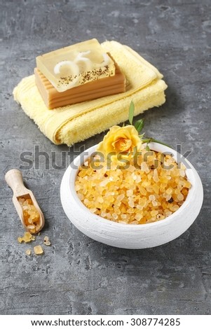 Bowl of yellow sea salt, towel and bar of handmade soap on gray stone background