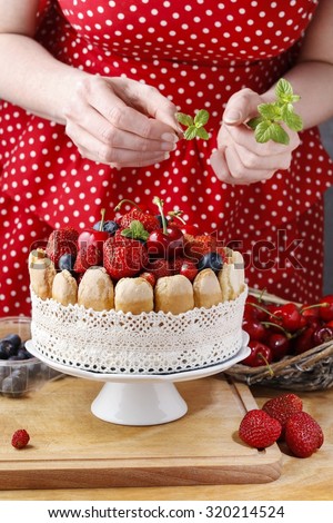 Woman decorating summer sponge cake with fruits on ceramic cake stand