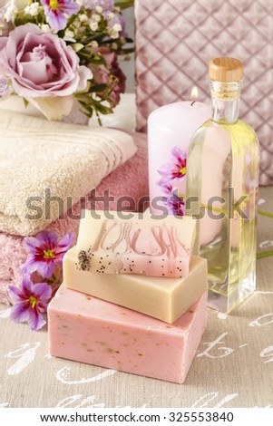 Bars of handmade soap and bottle of essential oil, scented candle and bouquet of flowers in the background.