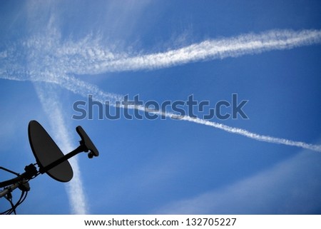 Contrails cross the sky above a satellite dish