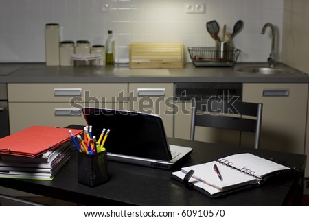 Working from home - a laptop, books, pens and an organizer on a kitchen table with kitchen in the background.