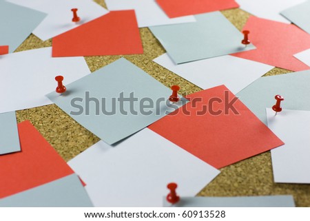 A bulletin cork board background with messy square pieces of white, blue and red posting paper, red pins.