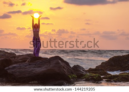 Woman stands at the rock and takes sunset sun in her hands