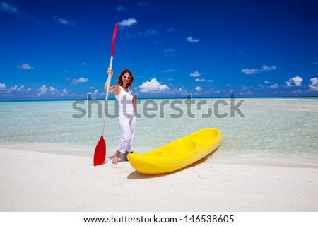 Young caucasian woman keeps paddle at the seashore near yellow kayak