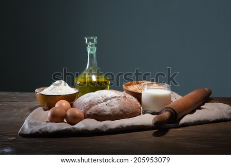Still life photo of bread and grain with milk and eggs at the wooden table