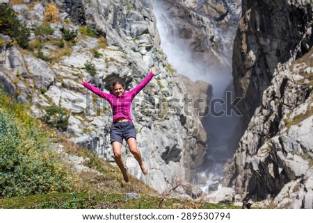 Caucasian woman is jumping in mountanis in front of big waterfall