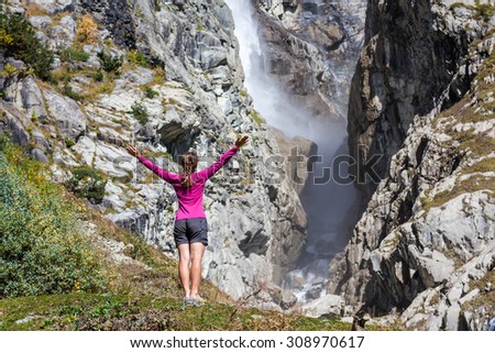 Cucasian woman is doing yoga exercises in mountanis in front of big waterfall