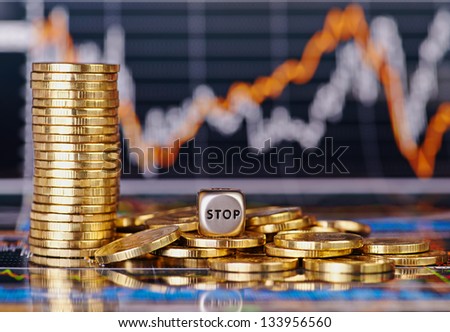 Dices cube with the word STOP golden coins and financial stock charts as background. Selective focus