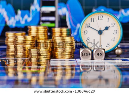 Stacks of golden coins, clock, dices cubes with the words STOP GO. The financial chart as background. Selective focus
