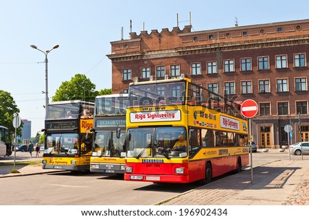 Riga, Latvia - May 25, 2014: Three yellow double-decker city sightseeing buses waiting for tourists on the Latvian Riflemen square in Riga, Latvia