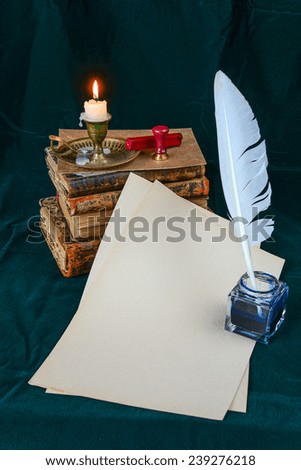 Still life with a letter, a pen, a lighted candle in copper candlestick and a pile of old books on a background of dark green velvet